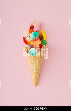 Gummibonbons in Waffel-Eiskegel auf pastellrosa Hintergrund. Kreatives Süßigkeiten-Dessertkonzept. Minimalistisches Design mit Gummigummi. Stockfoto