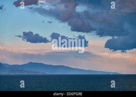 Dramatische Sturmwolken über ruhigem Meer bei Sonnenuntergang hinter dem Berghorizont Stockfoto