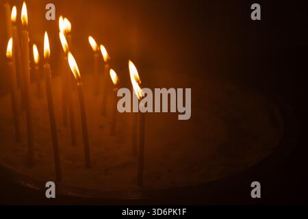 Mehrere brennende Gebetskerzen leuchten im Dunkeln der Kirche Stockfoto