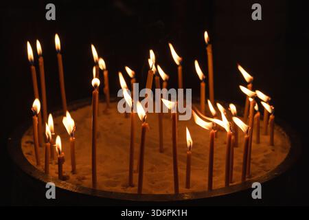 Heilige Kirchenszene mit einem runden Sandtablett und mehreren beleuchteten Gebetskerzen, die im Dunkeln leuchten Stockfoto