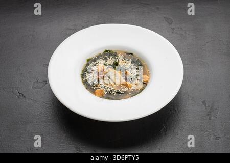Miso-Suppe mit Lachs, Wakam und Sesam in weißer Schüssel auf dunklem Steintisch Stockfoto