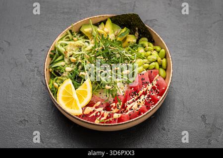 Lebendige Thunfisch-Poke-Schüssel mit Reis, Avocado, Edamame und Sesam auf dunklem Steinhintergrund Stockfoto