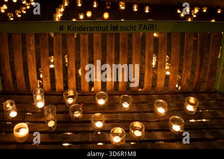 Bank mit Teelichtern in Gläsern steht in einem Meer aus weiteren Kerzen. Auf der Rückenlehne der Bank steht Kinderarmut ust nicht FAIR Kinderarmut ist kein Thema welches man auf die lange Bank schieben kann. Am Freitag, 21.11.2025 veranstaltet die Arche ein Lichtermeer vor der Arche Osnabrück an der Bremer Straße. Das Licht steht für die Kinder für ihre Träume, ihre Hoffnung, ihre Zukunft. Motto: Leere Köpfe, leere Mägen Kinder brauchen Perspektiven. Kinder dürfen nicht im Dunkeln bleiben Kinder gehören in den Mittelpunkt unserer Gesellschaft 24.11. Bundesweit der Aktionstag gegen Kinderarmut & Stockfoto