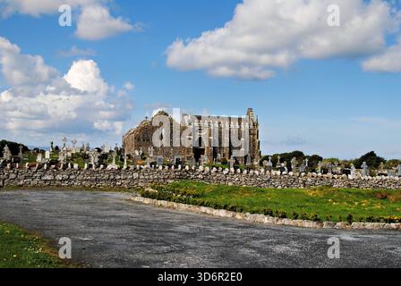 Alte Steinkirchenruinen und ein historischer Friedhof unter einem hellblauen Himmel mit verstreuten Wolken im ländlichen Irland. Stockfoto