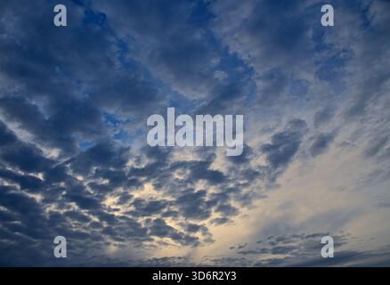 Bewölkter Abendhimmel mit dichten Stratocumulus-Wolken und Altostratformationen, die Flecken des blauen Himmels enthüllen und das wechselnde Wetter und das um einfangen Stockfoto