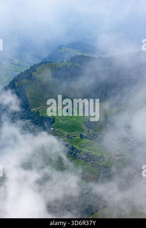 Aus der Vogelperspektive auf eine nebelige Berglandschaft am Stanserhorn mit grünen Feldern und einem kleinen Dorf. Stockfoto
