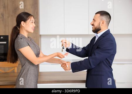 Ein männlicher Immobilienmakler gibt der Frau in der Küche den Schlüssel vom Haus Stockfoto