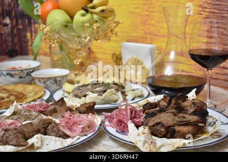 Gegrilltes Fleisch, einschließlich Lamm, Huhn und Lyulya-Kebab, Beshbarmak und Rotwein in Glaskaraffe Stockfoto