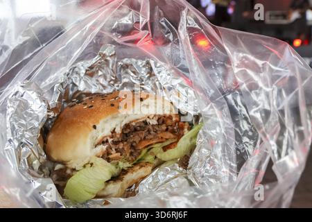 Zufriedenstellender Burger zum Mitnehmen, verpackt in Folie in Plastiktüte. Köstliche Fast Food-Mahlzeit, klassische Junk Food-Auswahl für schnelles Mittag- oder Abendessen unterwegs, Rea Stockfoto