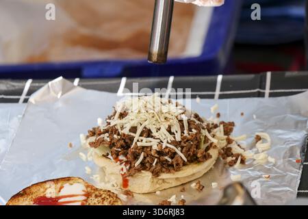 Köstliche Nahaufnahme des Küchenchefs, der herzhaften Käseeburger mit Hackfleisch und geriebenem Käse auf Folie zubereitet. Leckere Fast Food-Mahlzeit-Zubereitung in Profi Stockfoto