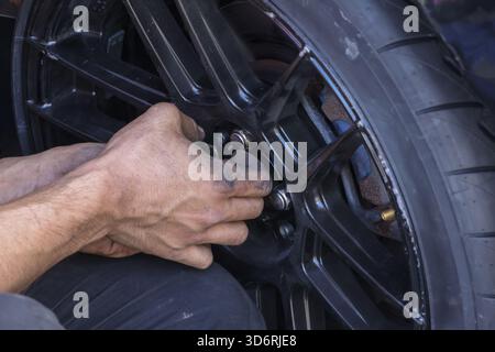 Ein fokussierter Mechaniker mit schmutzigen Händen führt Wartungsarbeiten und Reparaturen an den Rädern durch. Professionelle Autowartungsarbeiten an schwarzen Reifen in der Garage, sorgfältig festziehen Stockfoto
