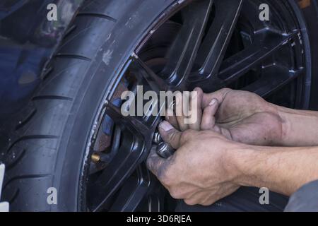 Nahaufnahme der Mechaniker, die sich auf die Arbeit konzentrieren, Festziehen der Radmutter am schwarzen Autorad. Autoreparaturservice in der Garage, Wartungsarbeiten am Fahrzeugreifen durchführen Stockfoto