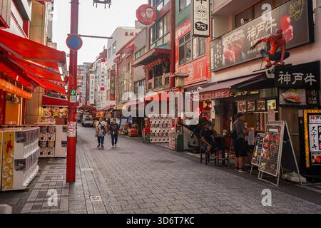 Touristen laufen auf der Straße durch Kobes Chinatown, Nankinmachi (南京町), umgeben von Geschäften und Imbissständen auf dem chinesischen Markt in Kobe City, Japan Stockfoto