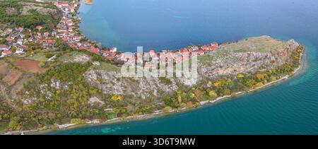 Blick aus der Vogelperspektive auf die felsige Halbinsel von Lin, umgeben von türkisfarbenem Wasser, Herbstbäumen und den Häusern am See. Stockfoto
