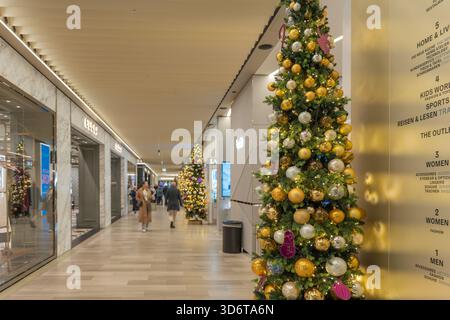 Deutschland Berlin 21. November 2025. Das Innere eines luxuriösen Einkaufszentrums ist mit hohen Weihnachtsbäumen und goldenen Ornamenten dekoriert. Shopper schlendern durch helle, Stockfoto