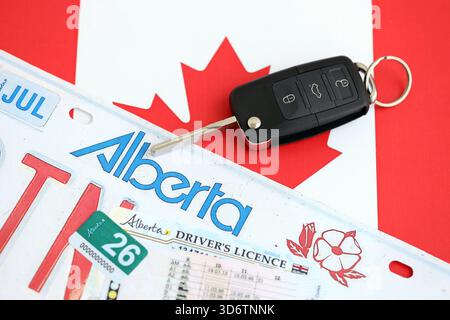 Alberta canadian Autokennzeichen und Zündschlüssel auf der Flagge von Kanada Nahaufnahme. Führerschein- und Zulassungskonzept Stockfoto