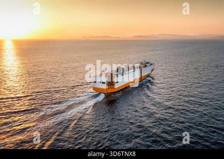 Luftaufnahme eines RORO-Transporterschiffs, das bei Sonnenuntergang mit Geschwindigkeit über den Ozean segelt Stockfoto
