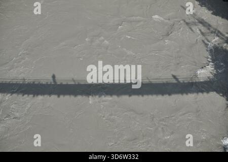 Fußgänger gehen über eine Brücke, ihre Schatten erstrecken sich über einen rauschenden Fluss. Die Szene fängt die dynamische Bewegung und Gelassenheit der Natur ein Stockfoto