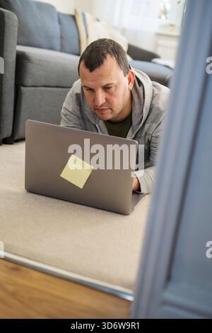 Ein Mann, der von zu Hause aus auf einem Laptop arbeitet und auf dem Boden liegt, von oben Stockfoto