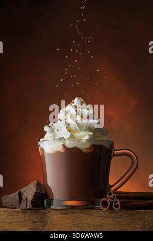 Geriebene Schokolade, die in eine Tasse heiße Schokolade mit Schlagsahne auf braunem Hintergrund gegossen wird Stockfoto