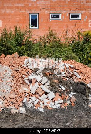 Haufen von Bauschutt - gebrochene Ziegelsteine und Betonblöcke, neues Gebäude im Hintergrund gebaut Stockfoto