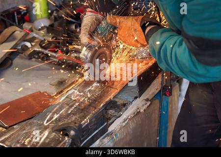 Mann, der in der Werkstatt mit Drehwinkelschleifer arbeitete, Details aus der Nähe, orangefarbene Funken flogen herum Stockfoto