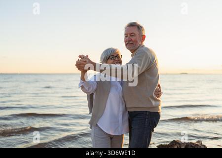 Bleiben Sie in Bewegung. Romantisches älteres Ehepaar, das gemeinsam am Strand im Freien tanzt. Glückliche lächelnde Familie pensionierter Mann Frau Ehemann Frau, die Spaß hat, die Zeit zusammen zu genießen. Familienmoment Love Care || Model veröffentlicht Stockfoto