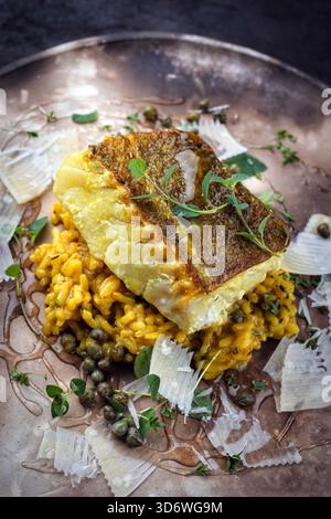 Gebratenes Fischfilet aus nordischem Kabeljau mit safran-Risottoreis, grünem Gemüse und Parmesankäse Stockfoto
