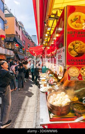 Geschäftige Straßenszene, Leute laufen entlang der Hauptstraße in Chinatown vorbei an dampfenden Knödeln in einem Bambustopf auf der Theke eines chinesischen Imbissstandes. Stockfoto