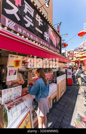 Die junge Japanerin bekommt ihr Wechselgeld, nachdem sie etwas Essen an der berühmten Kobe-Rindfleischtheke an der Ecke des Nankinmachi Plaza bestellt hat. Blauer Himmel. Stockfoto