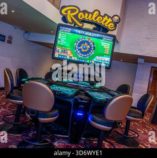 Moderner elektronischer Roulette-Tisch mit digitalem Jackpot-Bildschirm und Sitzplätzen im Casino-Innenraum, ideal für Spiele, Wetten und Unterhaltung. Stockfoto