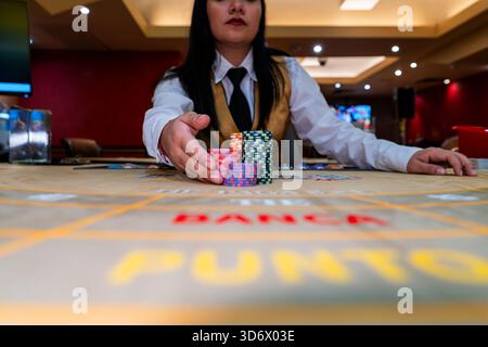 Der Baccarat-Dealer verschiebt Stapel von bunten Chips auf dem Casino-Tisch, die Spielaktionen, finanzielle Risiken, Wettatmosphäre und Spielumgebung zeigen. Stockfoto