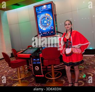 Frau in rotem Kostüm posiert neben elektronischem Roulette in Casino-Umgebung, zeigt Spielatmosphäre, Wettszene und Unterhaltungsumgebung. Stockfoto