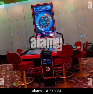 Elektronischer Roulette-Automat mit digitalem Display und roten Spielstühlen in moderner Casino-Umgebung, die Technologie und Wetteinstellungen zeigen. Stockfoto