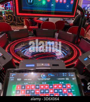 Elektronisches Roulette-Rad mit beleuchteten roten Lichtern, digitalen Konsolenbildschirmen und moderner Casino-Spieltechnologie in einer lebendigen Spielumgebung. Stockfoto