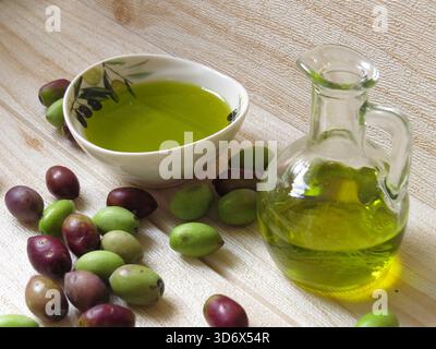 Natürliches, umweltfreundliches Olivenöl in Griechenland mit einer Flasche und einem kleinen Gericht, umgeben von frischen grünen und schwarzen Oliven auf dem Tisch. Stockfoto