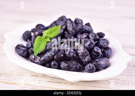 Geißblatt-Beeren auf einem Teller auf weißem hölzernem Hintergrund. Nahaufnahme. Stockfoto