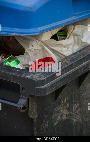 Schmutzige schwarze und blaue Industriekülle, die mit gemischtem Abfall, Müll und Plastiktüten überfüllt ist. Stockfoto