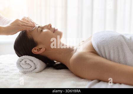 Junge Frau, die sanfte Stirnreinigung im Spa bekommt, die Hautpflege genießt Stockfoto