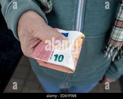 Nahaufnahme einer Person, die einen dicken Stapel von 10 Euro-Banknoten hält, die in einer direkten Geste zum Betrachter gestreckt wurde. Stockfoto