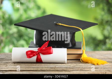 Graduierungskappe, Diplom und Bücher auf Holztisch vor verschwommenem Hintergrund, Großaufnahme Stockfoto