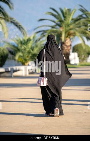 Arabisches muslimisches Mädchen in schwarzem Gewand auf der Straße. Silhouette einer arabischen Frau in traditionellem muslimischen schwarzen Hijab oder Jilbab. Rückansicht. Stockfoto