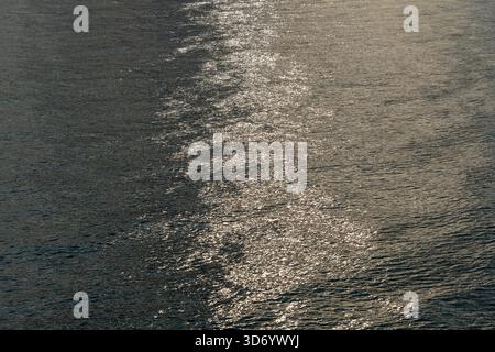 Wunderschöne Sonnenuntergangsreflexion funkelt auf winzigen Wellen der Meereswasserwelle im Hintergrund, Draufsicht. Die Textur des Meerwassers. Stockfoto