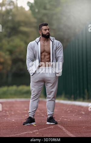 Muskulöser Mann steht auf einer Laufbahn in sportlicher Kleidung. Er scheint konzentriert und entspannt zu sein und hebt seine Fitness-Reise hervor. Die Hintergrundleistung Stockfoto