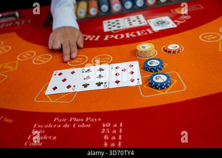 Händlerhand zeigt auf Karten auf einem karibischen Pokertisch mit Casino-Chips, Spielkonzept, Wetten, Strategie, Risiko und Casino-Unterhaltung. Stockfoto