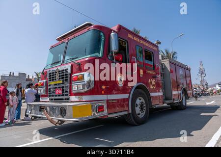 Feuerwehrauto fährt in einer Bürgerparade, während Feuerwehrleute und Zuschauer während einer öffentlichen Veranstaltung in Peru auf einer städtischen Straße beobachten Stockfoto
