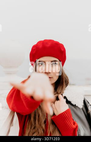 Frau Baskenmütze rot. Selbstbewusste Frau in roter Baskenmütze zeigt sich draußen in die Kamera. Stockfoto