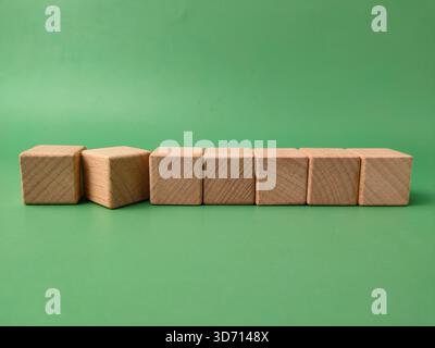 Das Bild zeigt sieben natürliche, unfertige Holzwürfel, die in einer Linie auf grünem Hintergrund angeordnet sind. Stockfoto