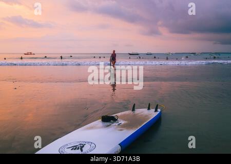 Surfer machen einen gemütlichen Spaziergang am Jimbaran Beach am Nachmittag, dem 5. Oktober 2025, in Bali, Indonesien Stockfoto