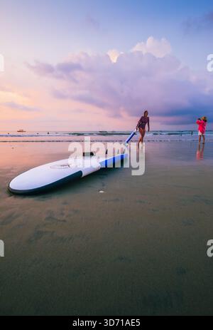 Surfer machen einen gemütlichen Spaziergang am Jimbaran Beach am Nachmittag, dem 5. Oktober 2025, in Bali, Indonesien Stockfoto